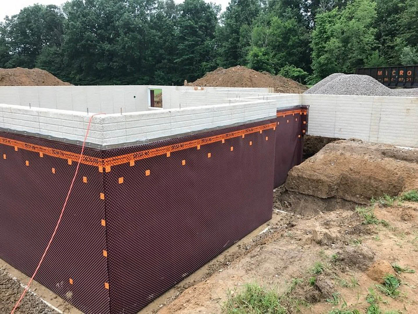 Framed custom home under construction surrounded by dirt, trees, and construction materials; exposed composite walls and foundation visible.
