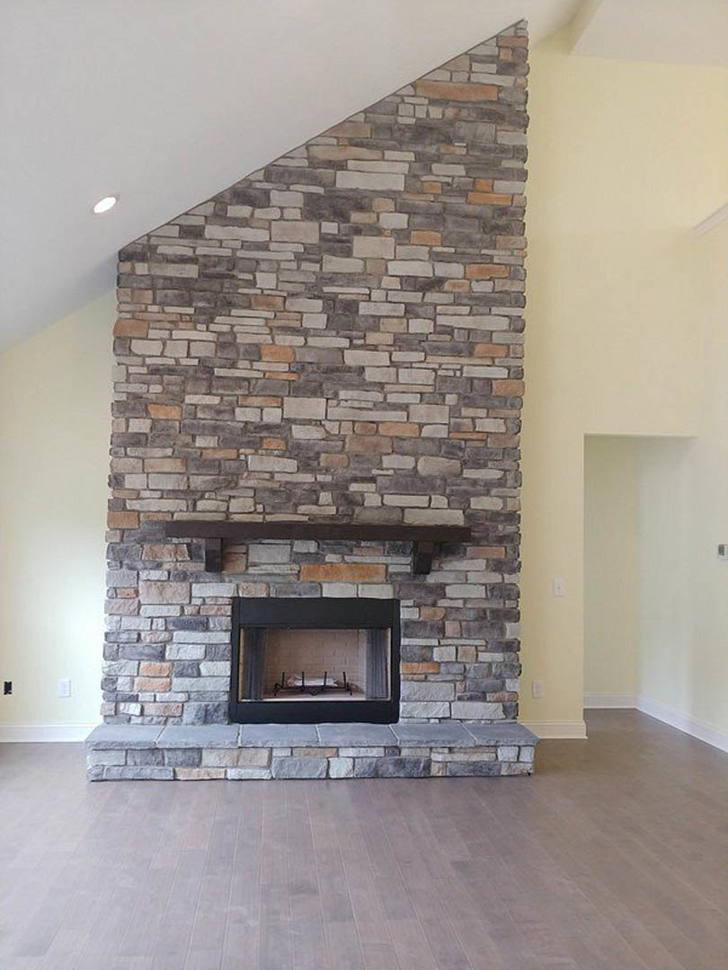 Stone fireplace with black metal frame and wood mantel, set against a white wall with black trim, hardwood flooring in foreground