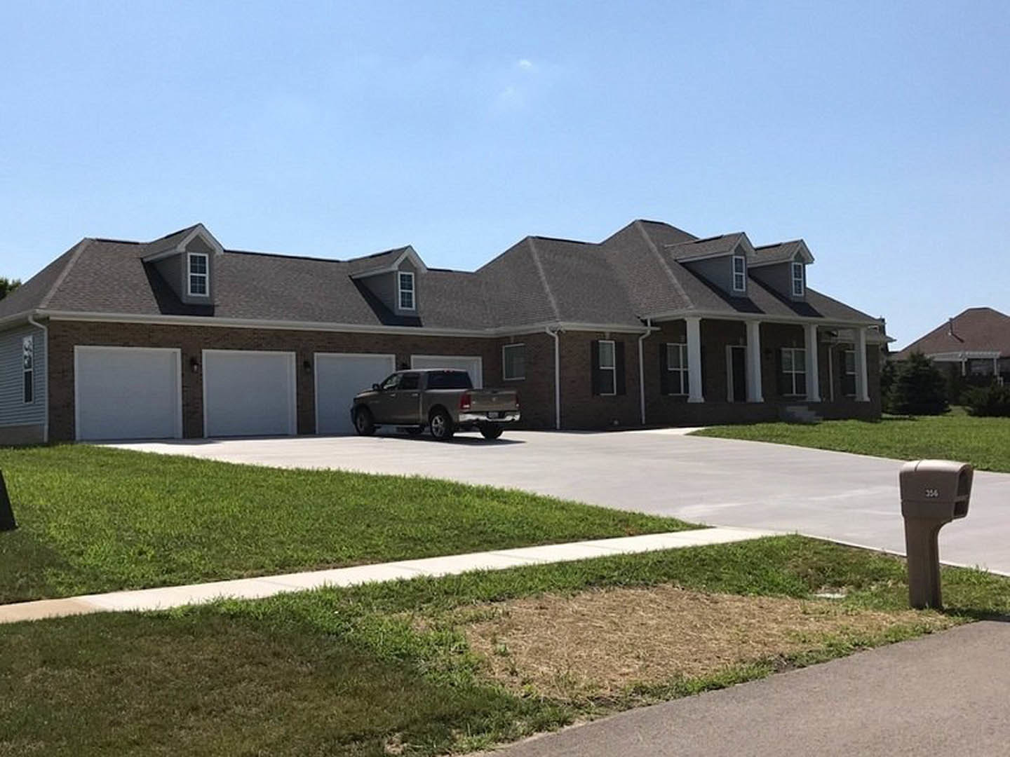 Two-story house with gray siding, white trim, and large windows, manicured lawn, concrete driveway, pickup truck parked in front