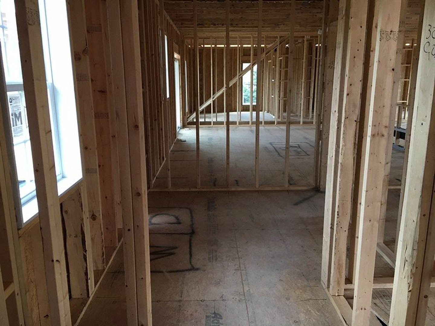 Exposed wood framing and beams in a house under construction, unfinished walls and ceiling, subfloor marked with construction graffiti
