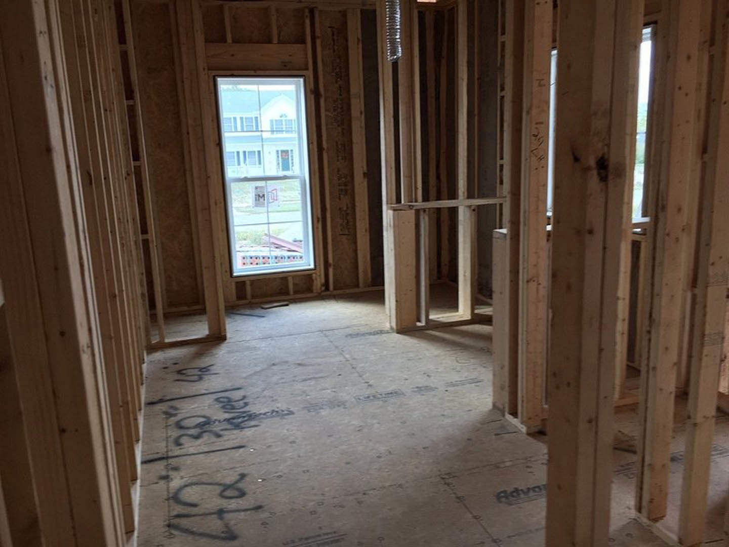 unfinished room with exposed wood framing, rectangular window with a sign, concrete floor marked with black writing, close-up of paper on floor