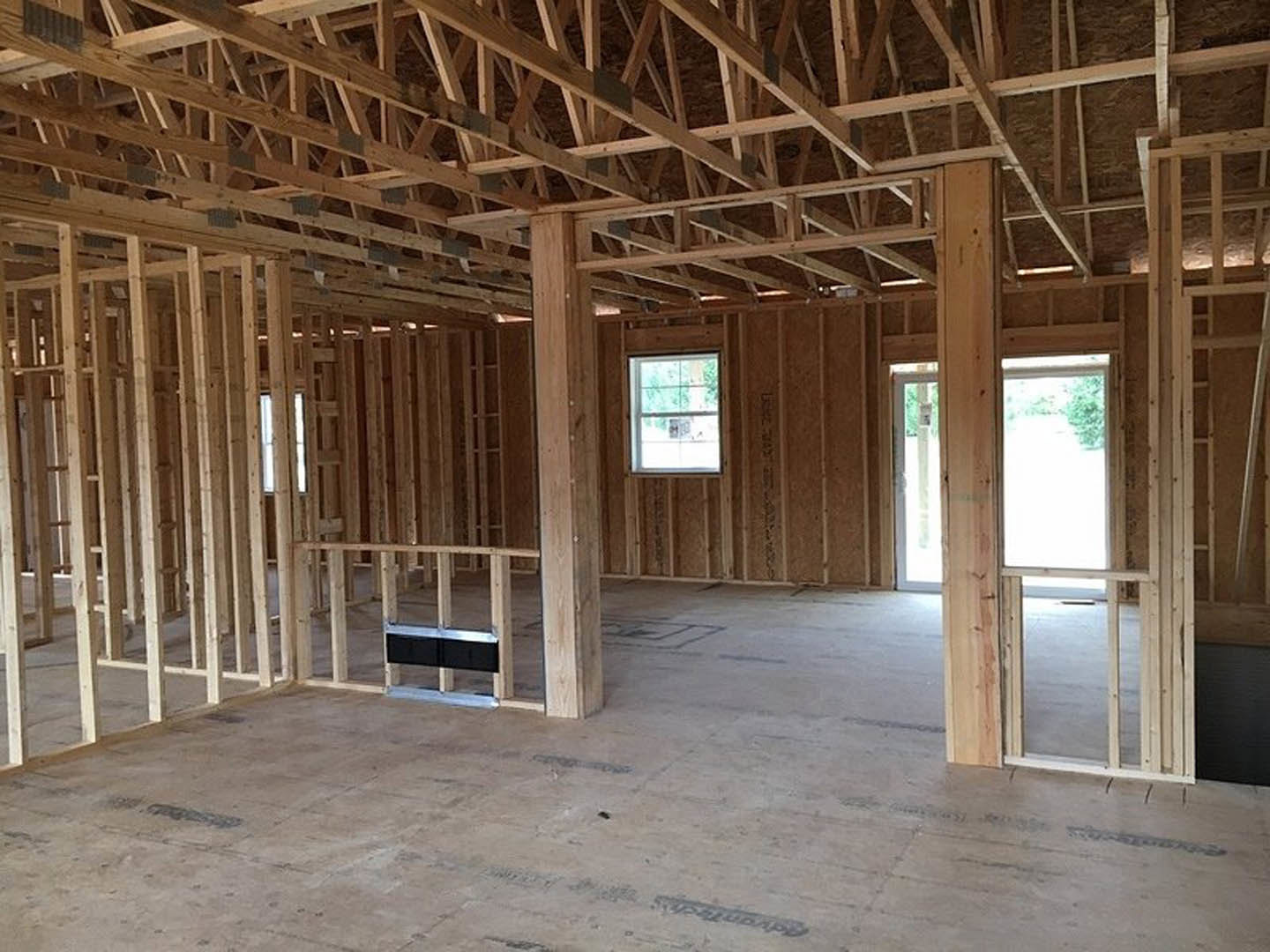 Living room with exposed wood ceiling beams, large window overlooking outdoor greenery, light hardwood floors, and neutral walls.