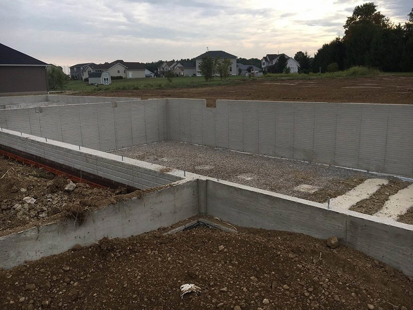 Concrete foundation slab surrounded by dirt and grass in an open field under a cloudy sky