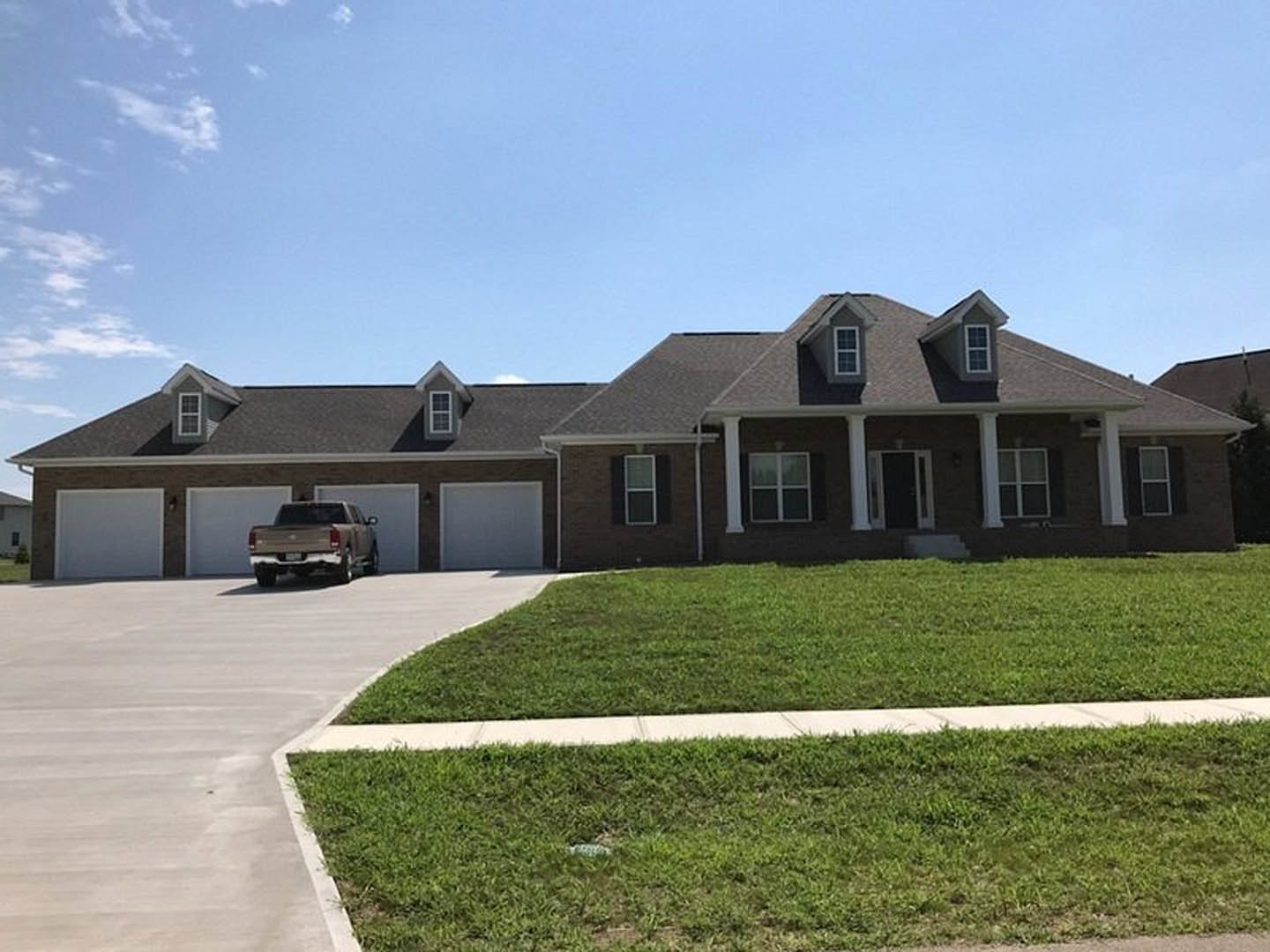 Two-story house with white siding, attached garage, concrete driveway, green lawn, and pickup truck parked near the curb under a partly cloudy sky