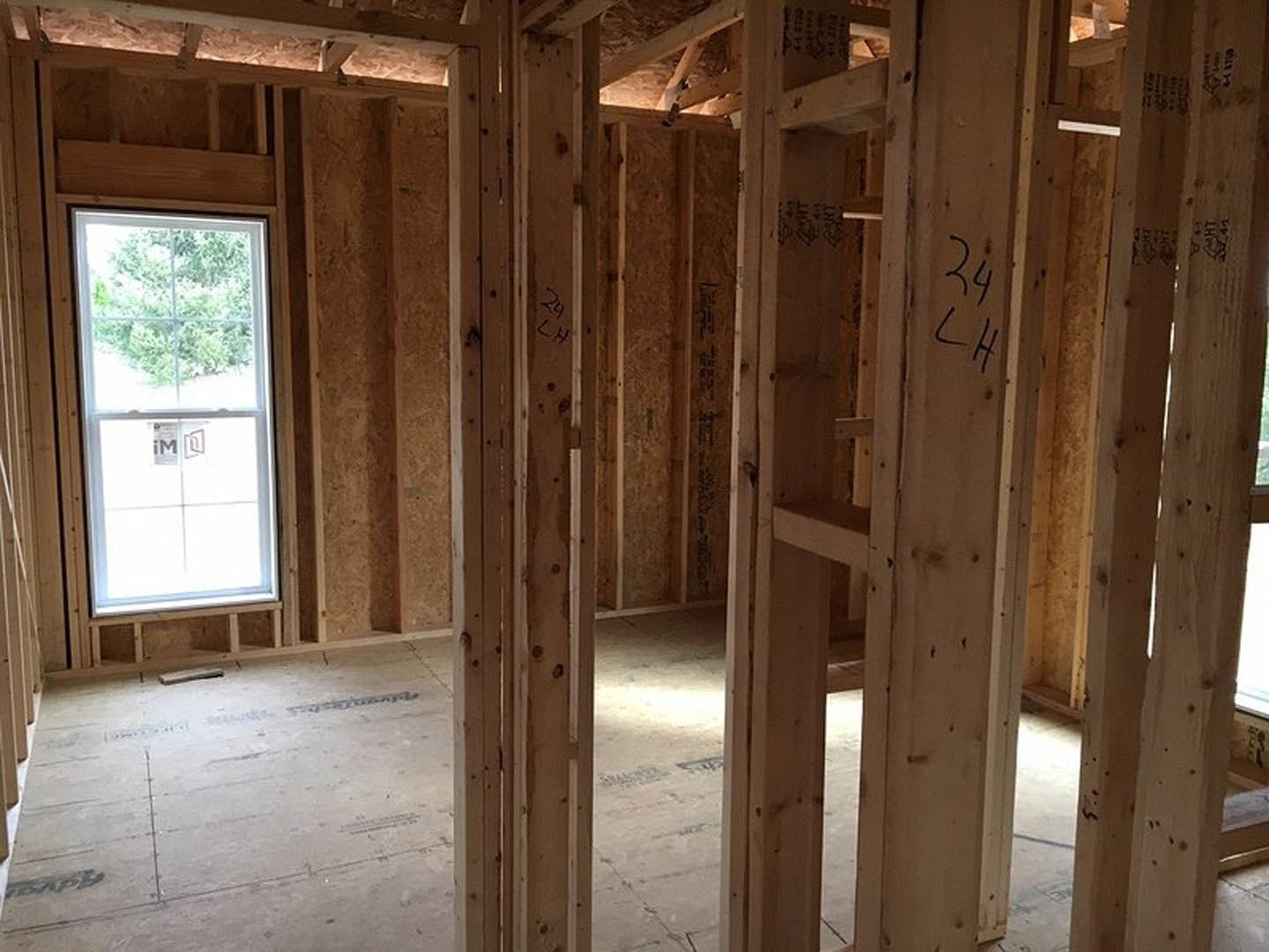 Wood-framed room with exposed beams, doorway leading to adjacent space, window displaying a sign, close-up views of numbers and logo on construction materials