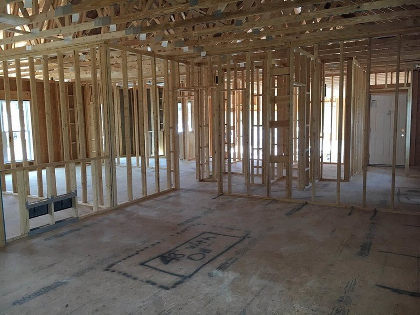 Wood-framed room with exposed ceiling beams, concrete floor, white door illuminated by light, close-up of ground drawing, and metal floor grate