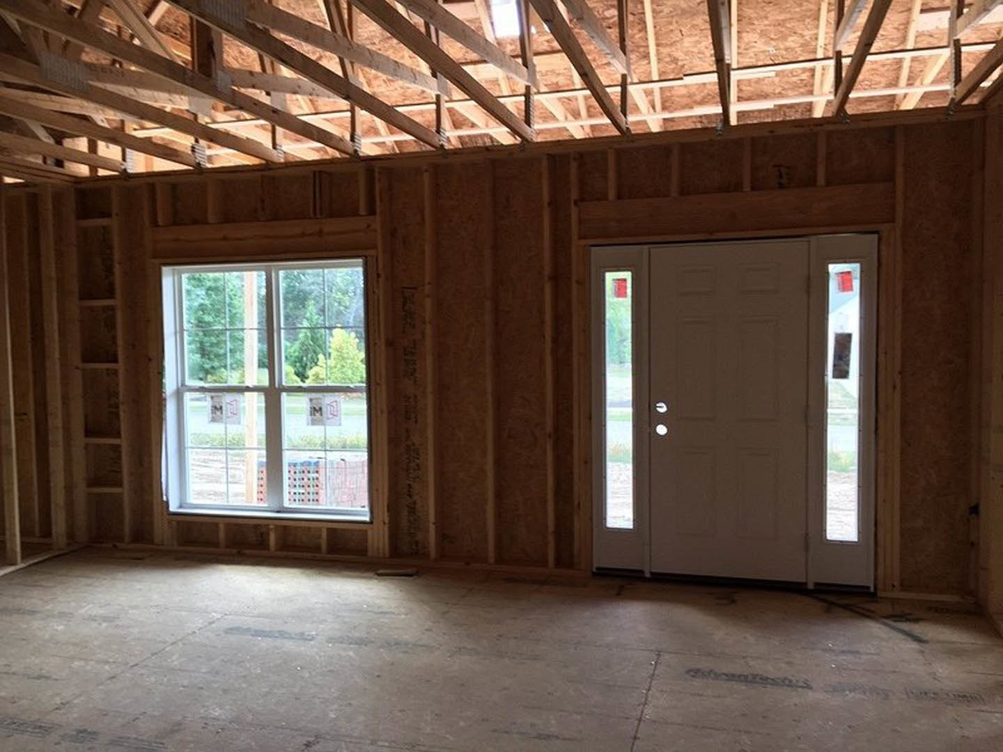 White paneled door with glass inserts, large clear window, exposed wooden ceiling beams, sunlight illuminating hardwood floor
