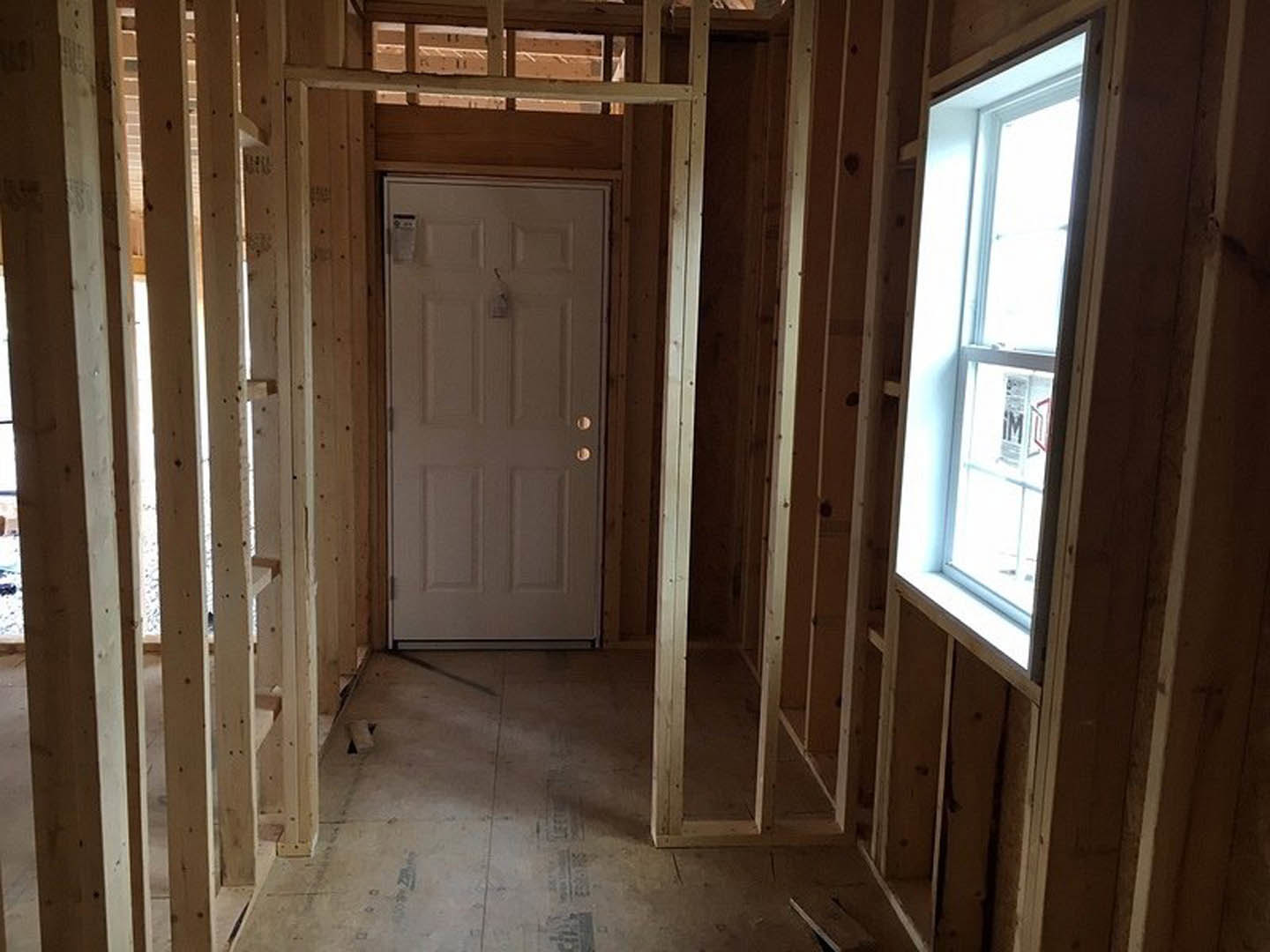 Sunlit room featuring a white door with a lock, large window, wooden floor, and close-up of a wooden railing against plaster walls.