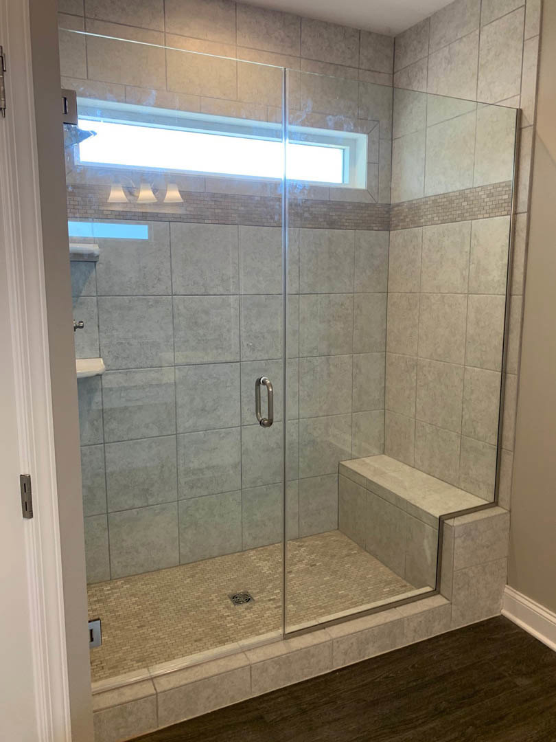 Glass shower enclosure with built-in bench, large window, and light-colored tile flooring