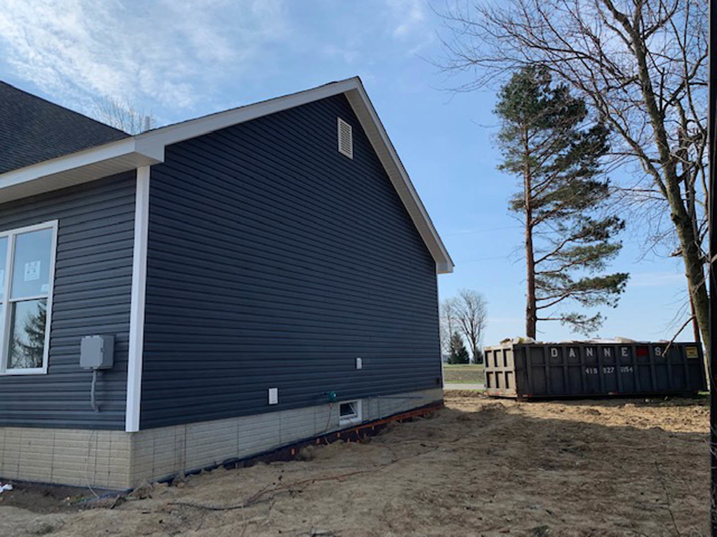 Modern home with flat roof, white siding, large windows with white frames, tree in front yard, construction dumpster on driveway