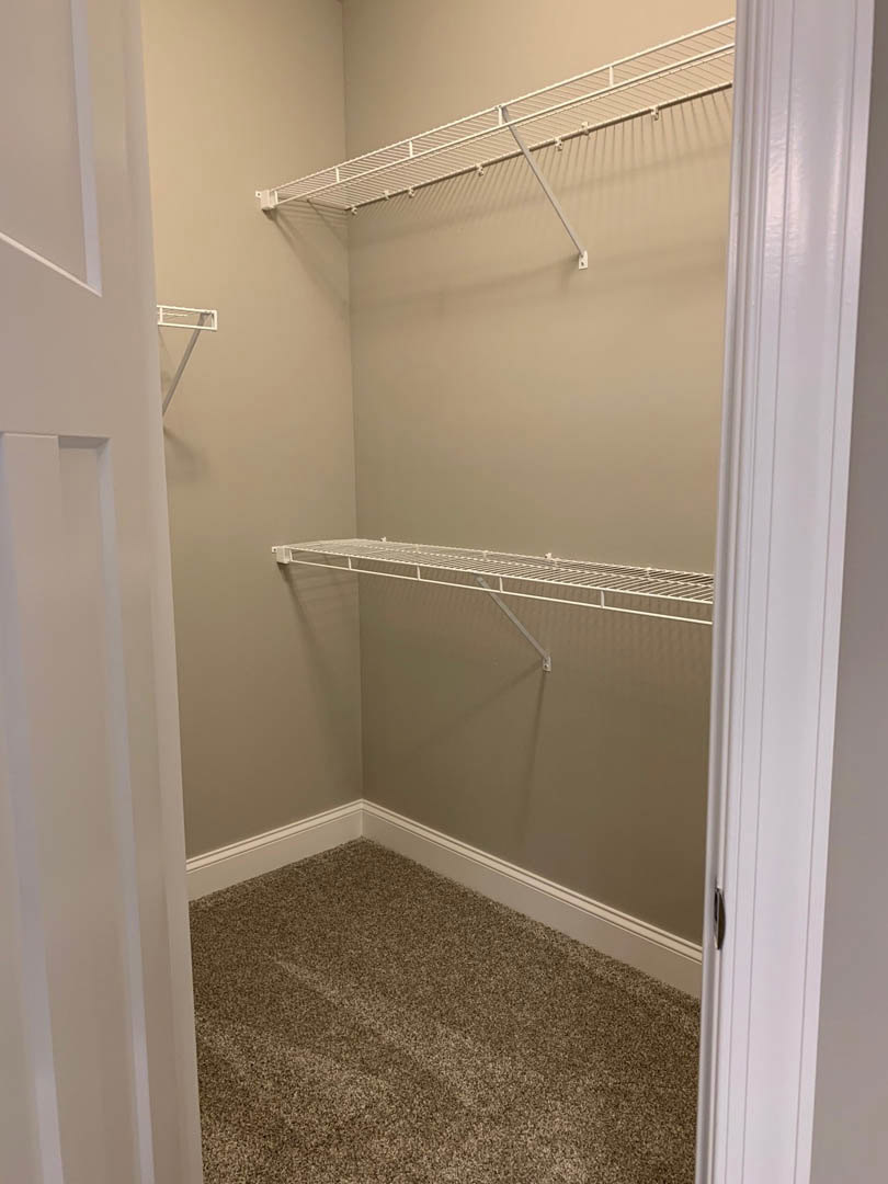 Walk-in closet with white shelving, metal hanging rods, and light-colored carpet flooring