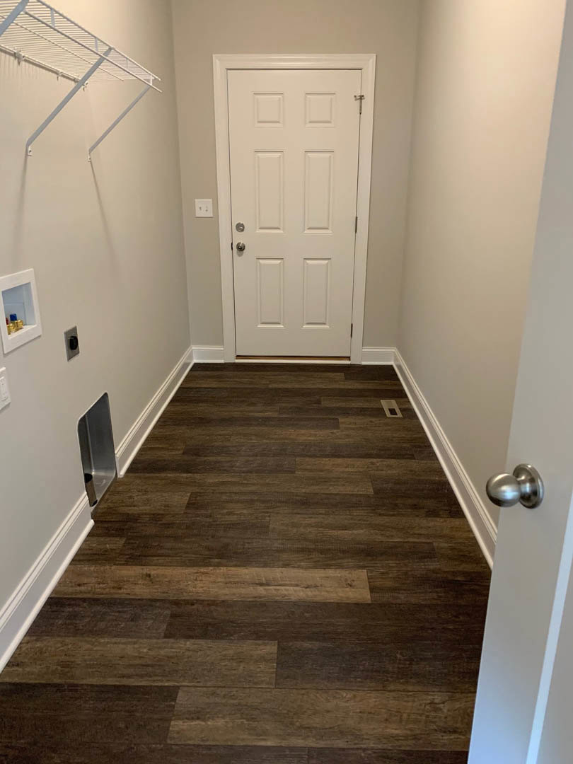 Hallway with light wood flooring, white walls, white door with silver handle, built-in shelf holding decorative objects