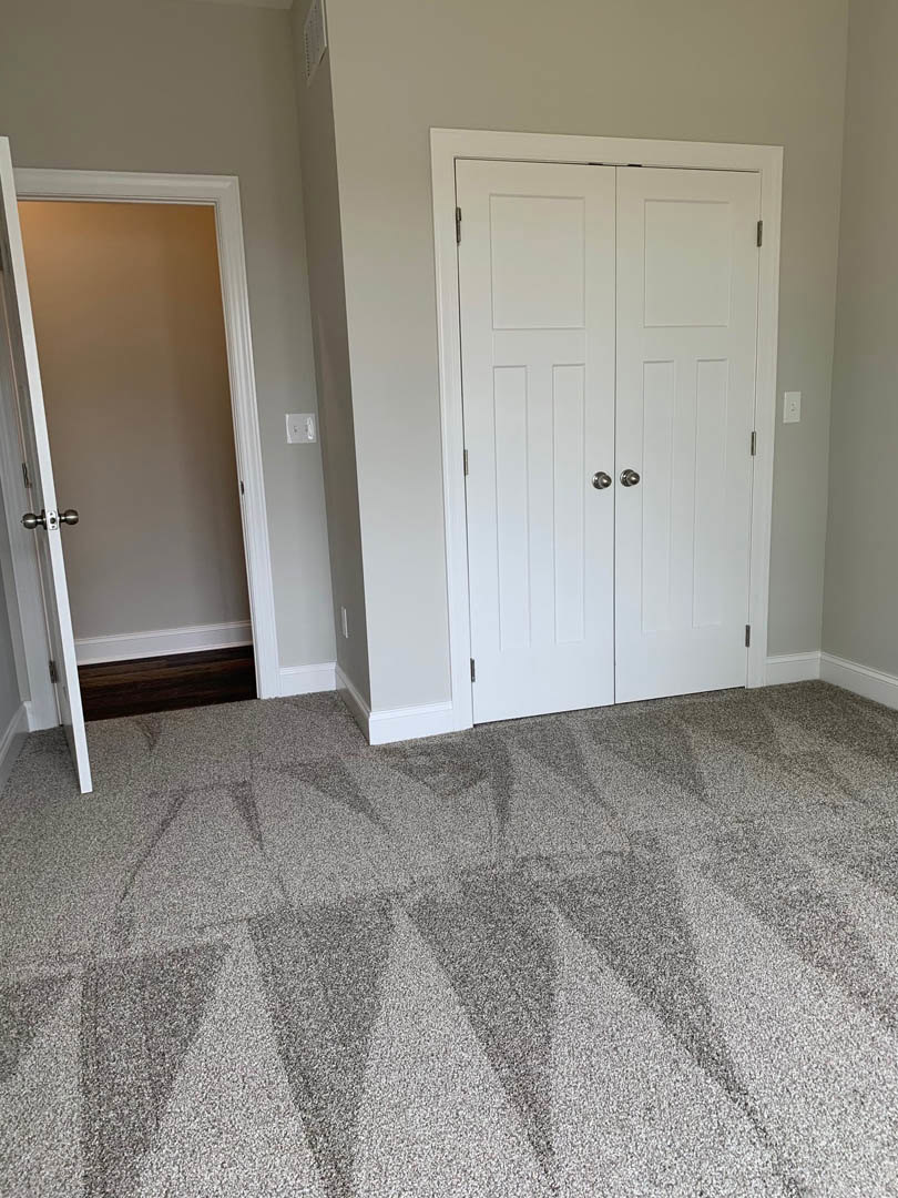 White paneled door with silver handle, geometric patterned carpet in neutral tones, smooth plaster walls, soft overhead lighting