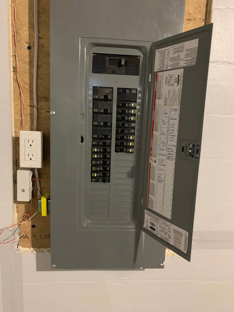 Open grey electrical panel mounted on white wall, showing multiple switches and wiring inside