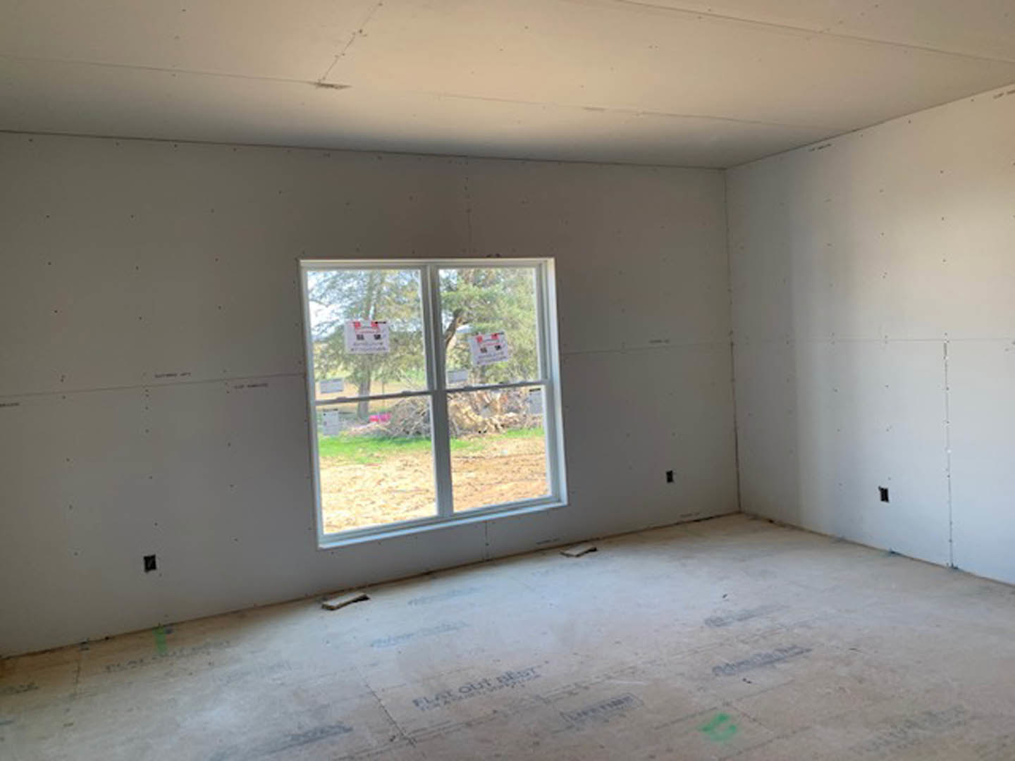 Sunlit room with large window, smooth concrete floor, white plaster walls, and unfinished ceiling