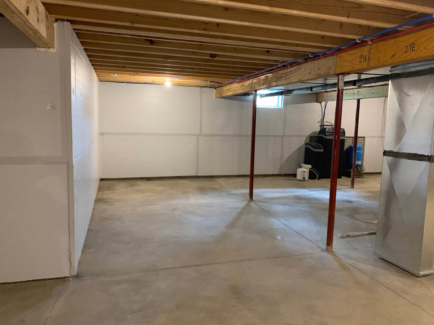 Basement with exposed wooden beam and wood plank ceiling, concrete floor with metal support pole, white container with blue cap, glass wrapped in black tape, close-up of mechanical