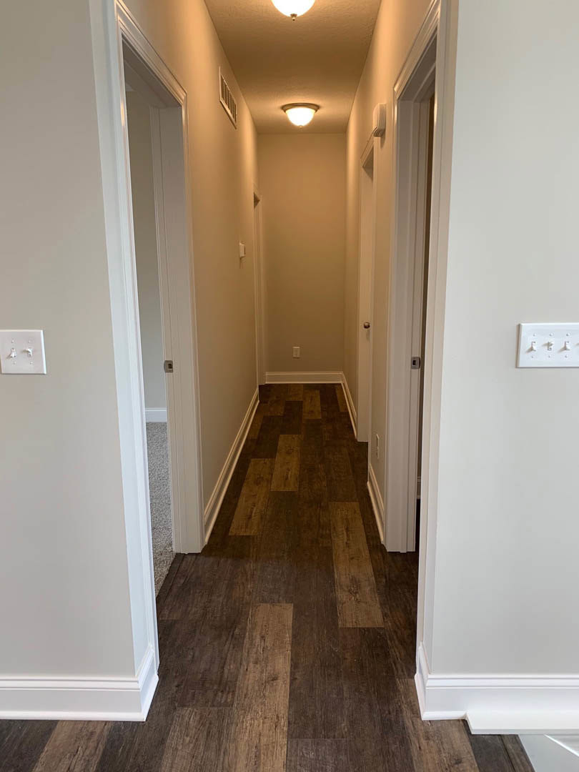 Hallway with dark wood flooring, white baseboards, white plaster walls, three-switch light switch plate, and ceiling light fixture