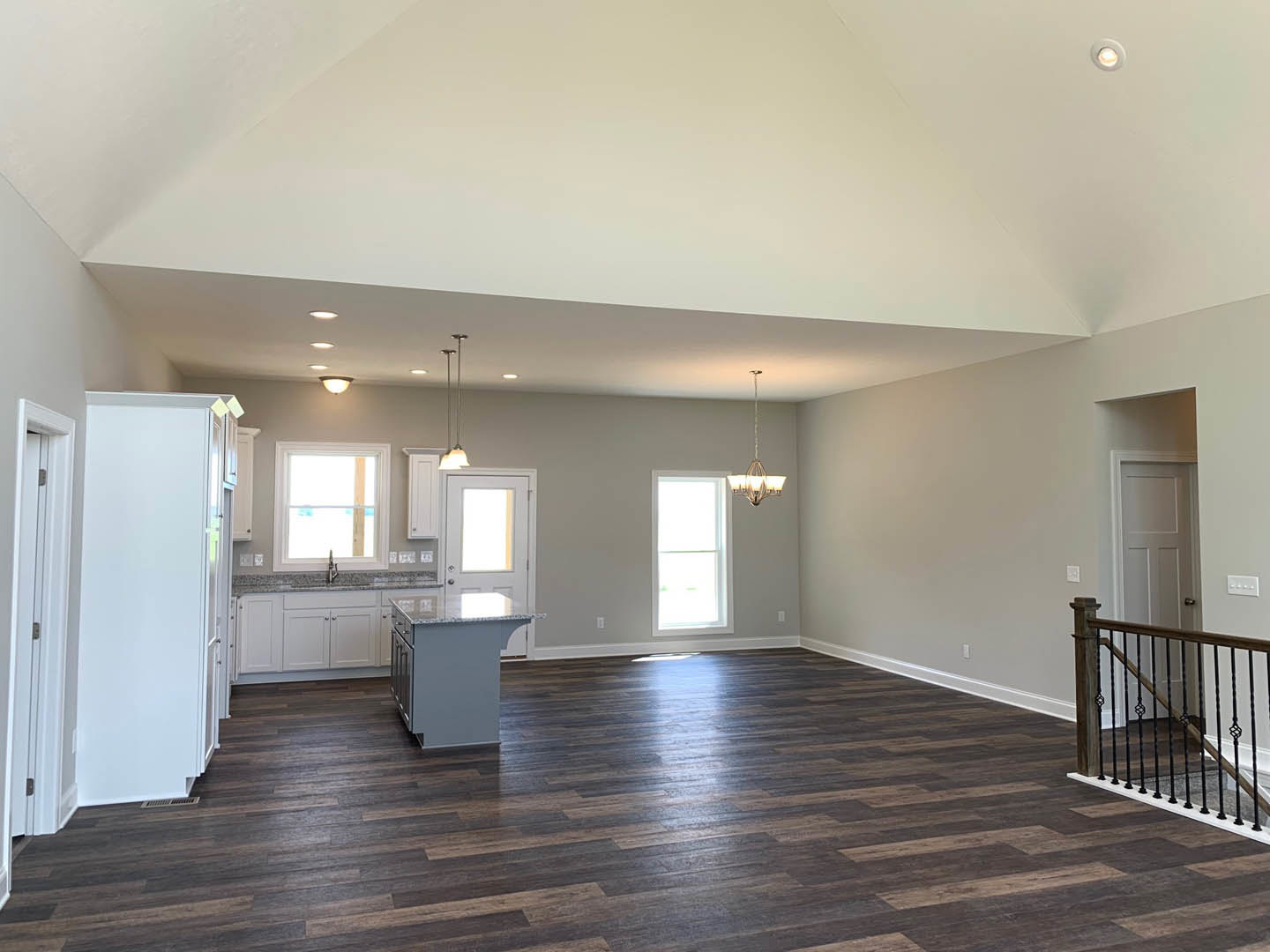 Open-concept kitchen with glass-topped island, hardwood floors, white walls, and large window; close-up of staircase and white door visible