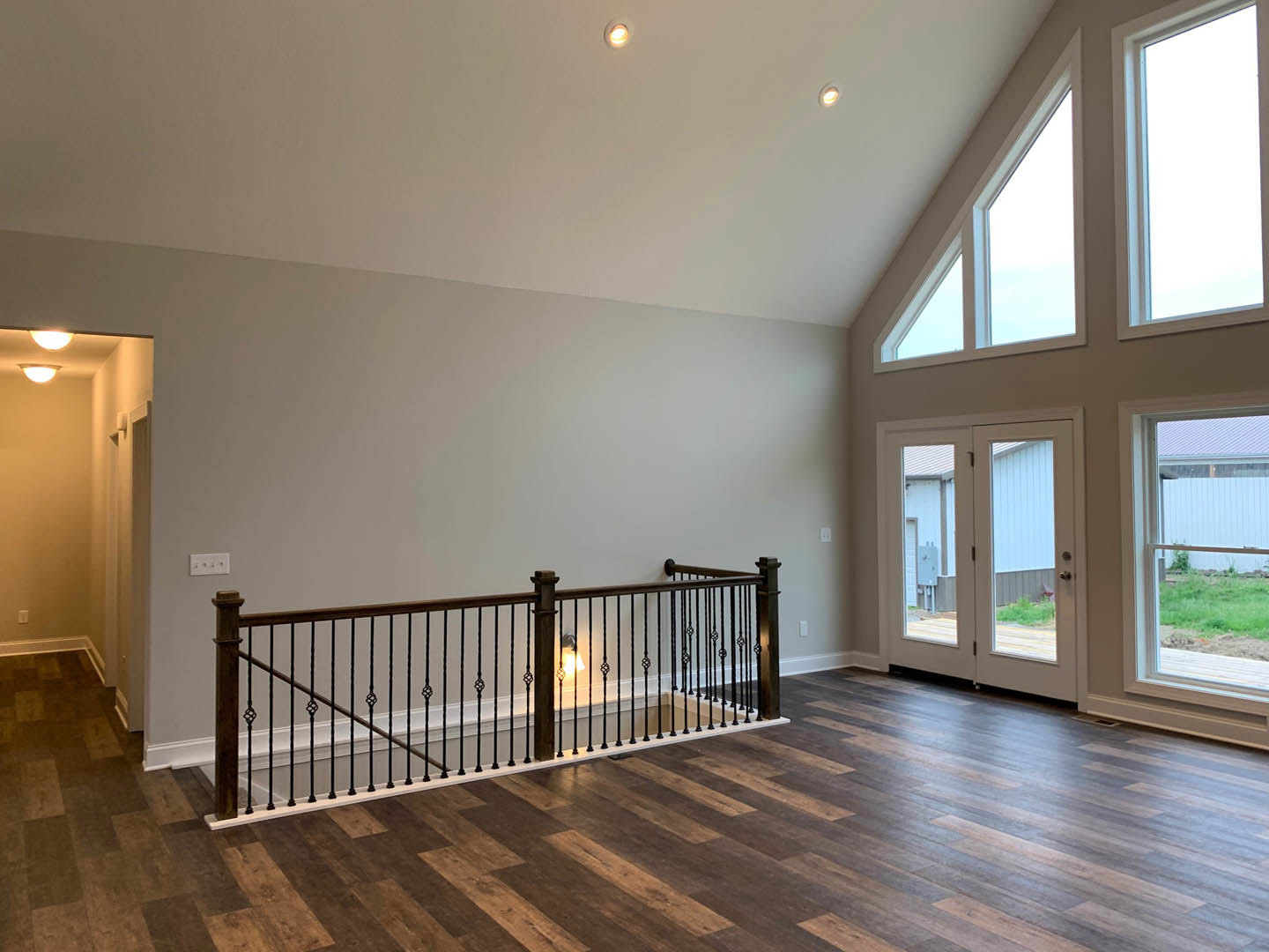 Open living area with light hardwood floors, black metal staircase railing, large window, and double glass-paneled doors