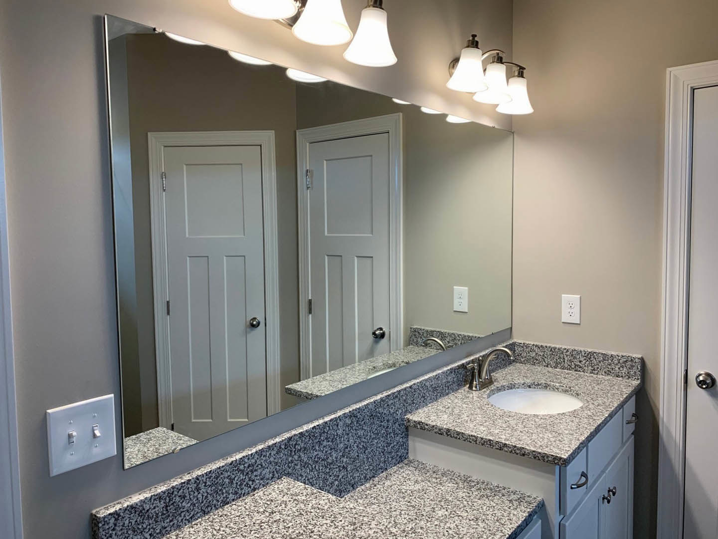 Bathroom with expansive wall mirror above white countertop, chrome faucet, tiled backsplash, and white door featuring black handle and silver knob