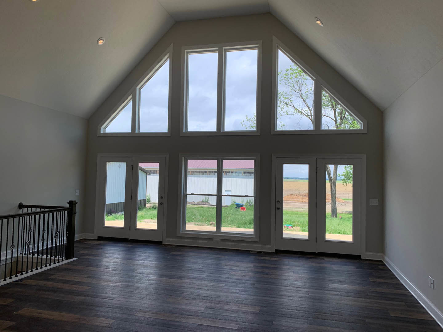 Spacious interior featuring dark hardwood floors, prominent staircase with detailed railing, multiple large windows allowing natural light, and views of green lawn outside