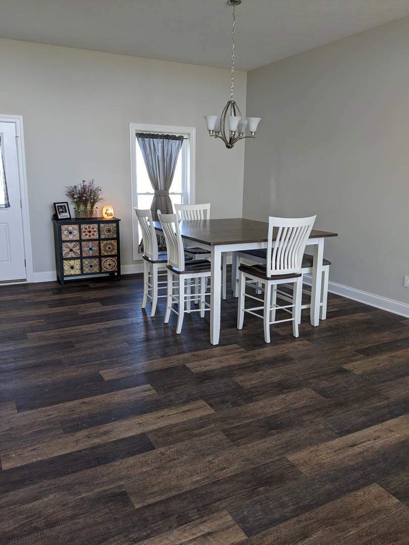 Hardwood floor dining room with white chairs around a wooden table, neutral walls, cabinet, and light curtains