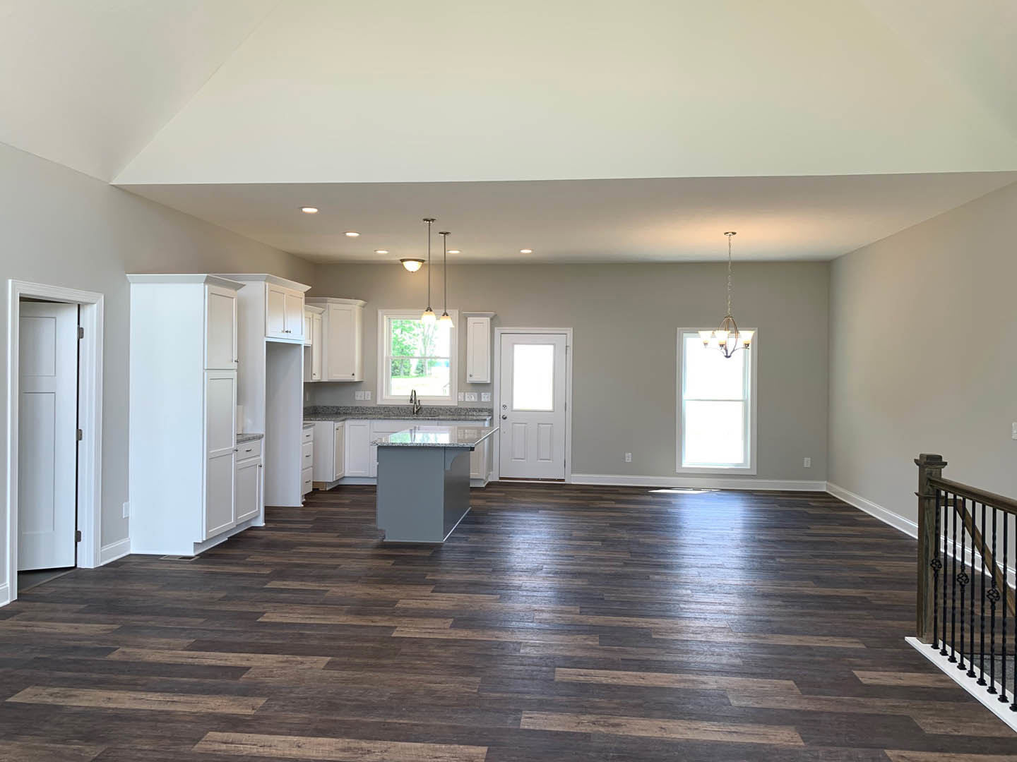 Open-concept kitchen and dining area featuring a marble-topped island, hardwood floors, white cabinetry, a close-up of a modern railing, large windows, and a white door with glass