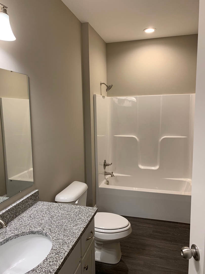 Modern bathroom with white tile walls, glass shower enclosure, wall-mounted sink with chrome faucet, toilet beside bathtub, large mirror above vanity, and recessed lighting