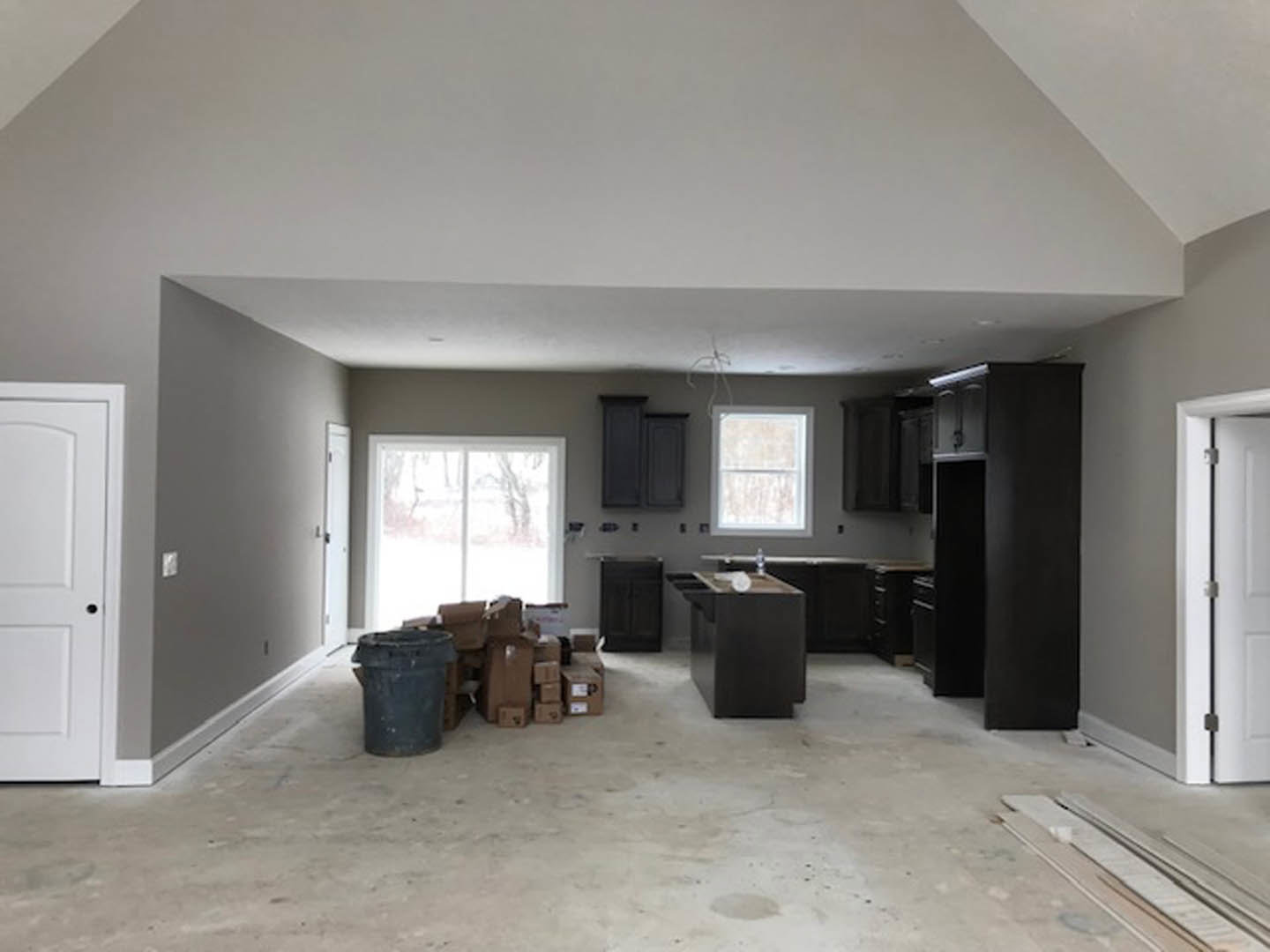 Spacious kitchen featuring extensive cabinetry, light countertops, black trash can, window with outdoor view, close-up of a door, and sleek black appliances.