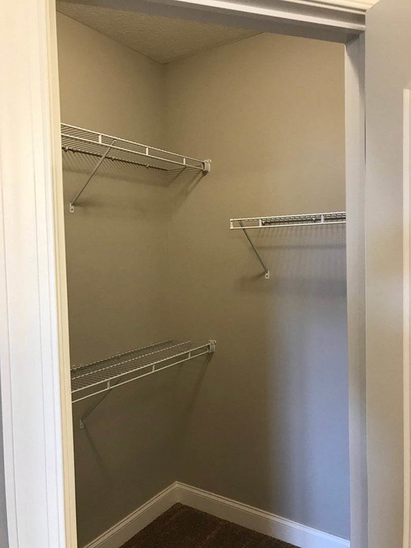 Walk-in closet with white metal shelving, hanging rod, carpeted floor, and overhead ceiling light