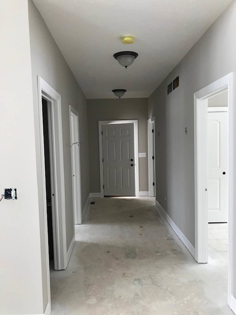 Hallway with smooth white walls, grey door featuring black hardware, two modern ceiling light fixtures, and polished concrete flooring