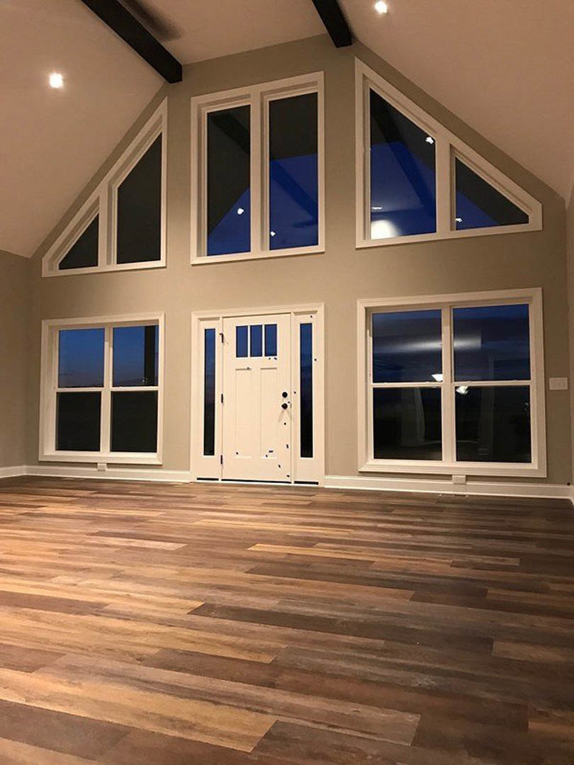 White paneled door and large windows with white frames, hardwood floor, white ceiling, and neutral walls in a bright interior room