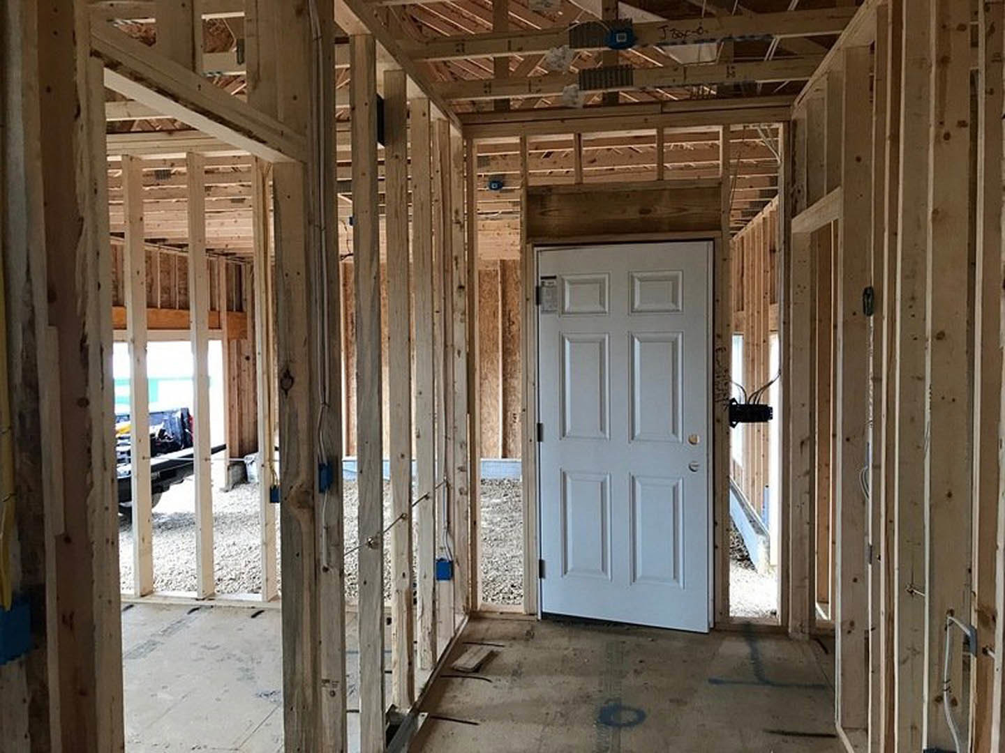 Unfinished room featuring a white door, wood-paneled wall, exposed ceiling beams, construction materials, and visible wiring.