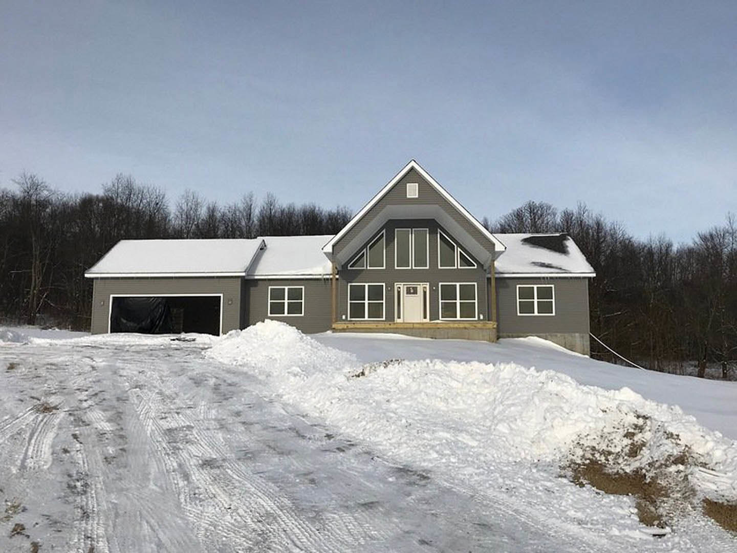 Two-story house with white door and window, snow covering ground and piled near entrance, trees visible behind roof, person in black pants standing outside