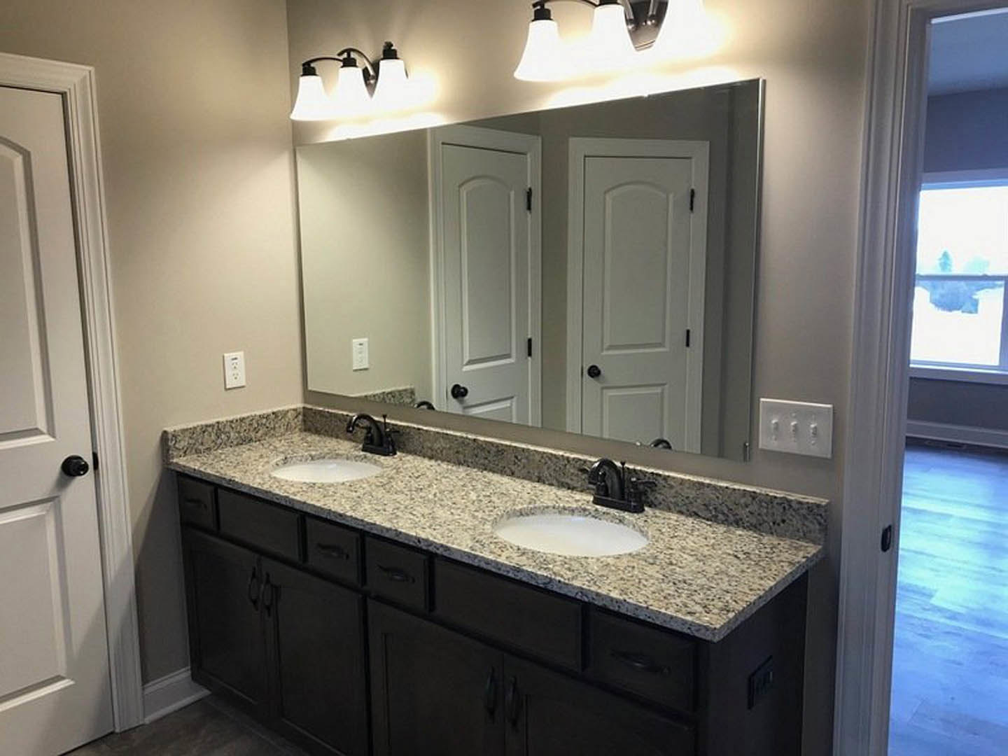 Double vanity bathroom with white stone countertop, two undermount sinks, large wall mirror, black faucet fixtures, light sconces, and tile backsplash