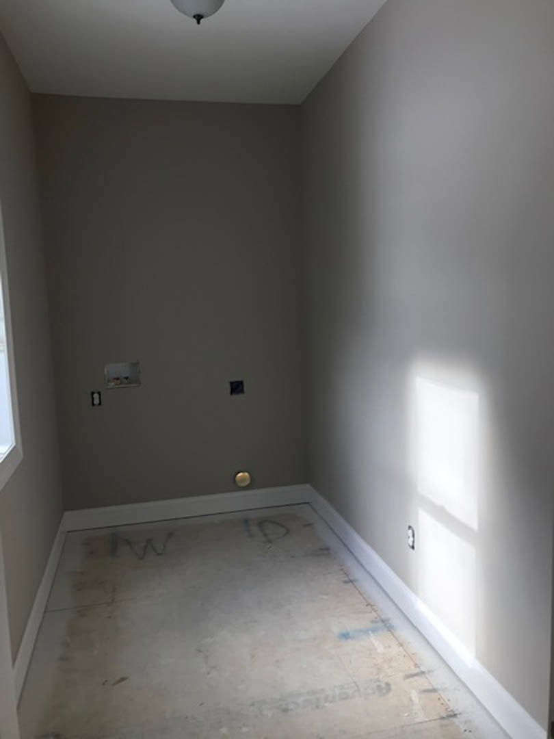 Concrete floor with hand-drawn markings, plaster walls, wall-mounted light fixture, and a wooden shelf in a residential interior.