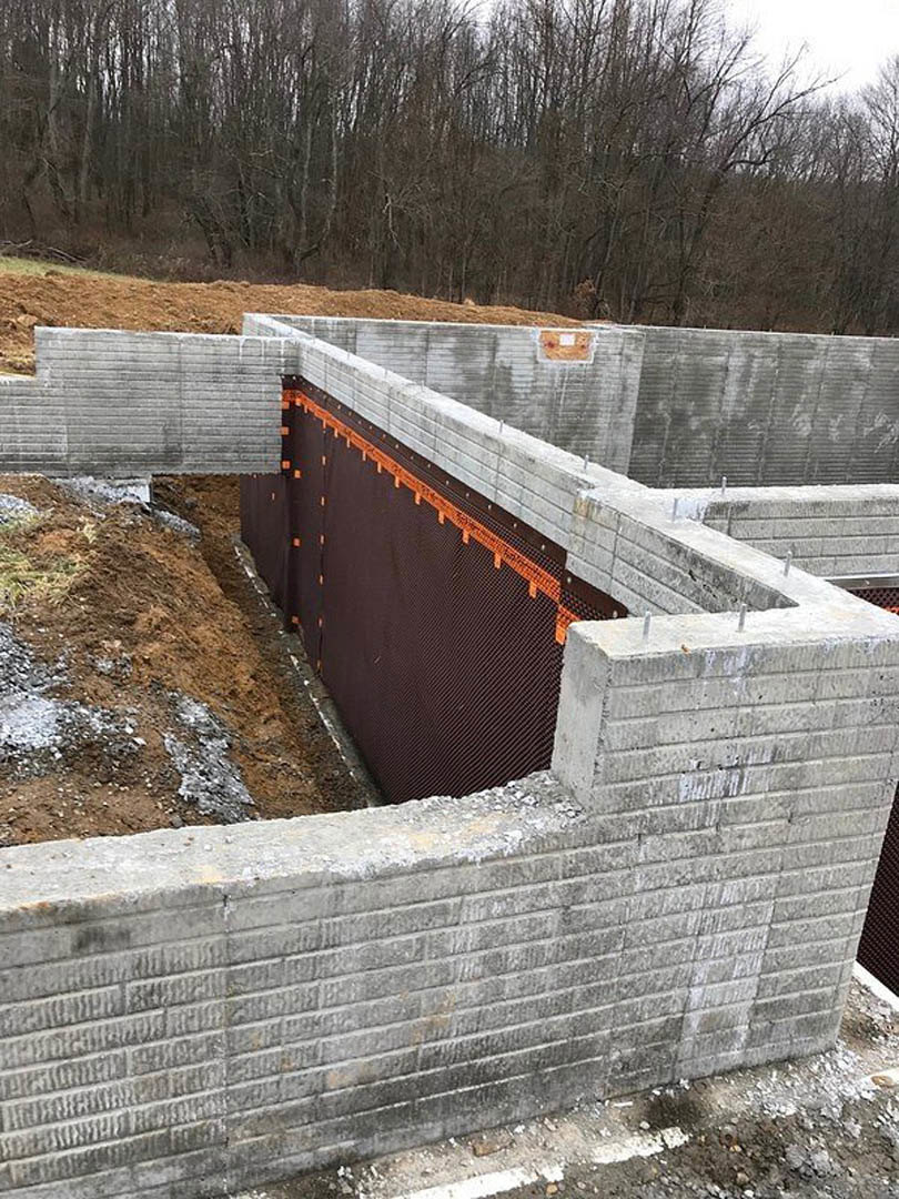 Concrete foundation with brown metal wall, surrounded by bare trees and winter ground, under a cloudy sky