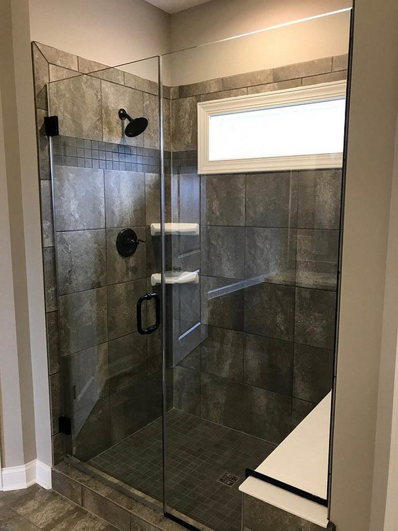 Glass shower enclosure with chrome shower head, white rectangular niche set in brick-patterned tile wall, black metal towel bar, black framed mirror, and black pendant light