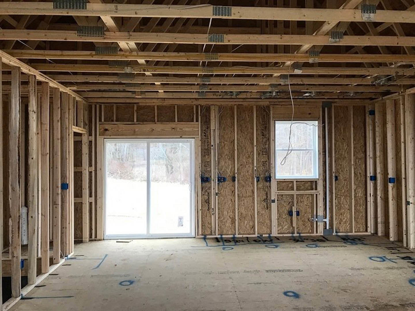 Living room with exposed wooden ceiling beams, large windows framing snowy landscape, white rope detail on window, wood-paneled walls, and adjacent door.