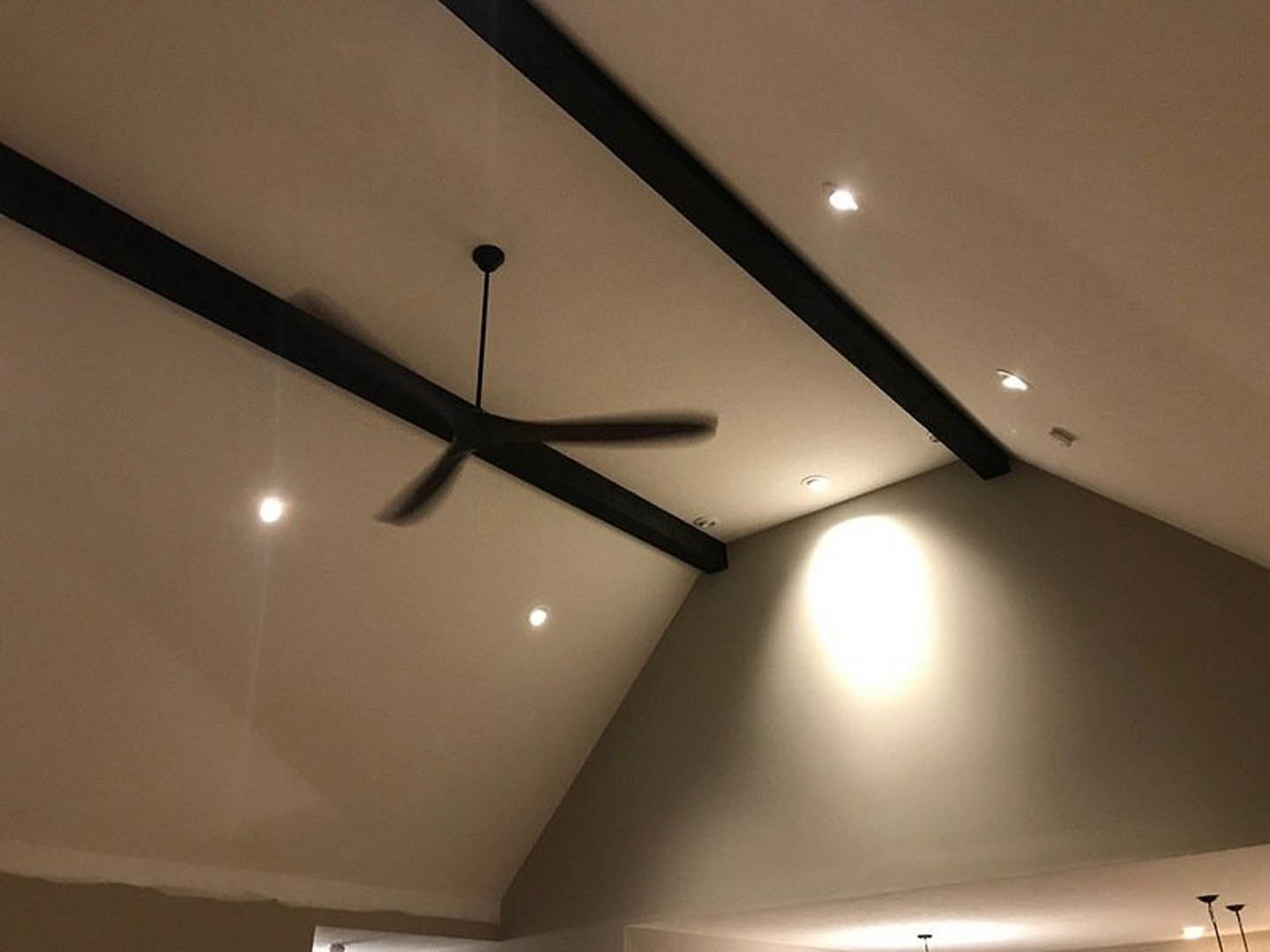 Ceiling fan with brushed metal blades mounted on white ceiling, recessed lighting, white walls, and black wall clock in modern living room.