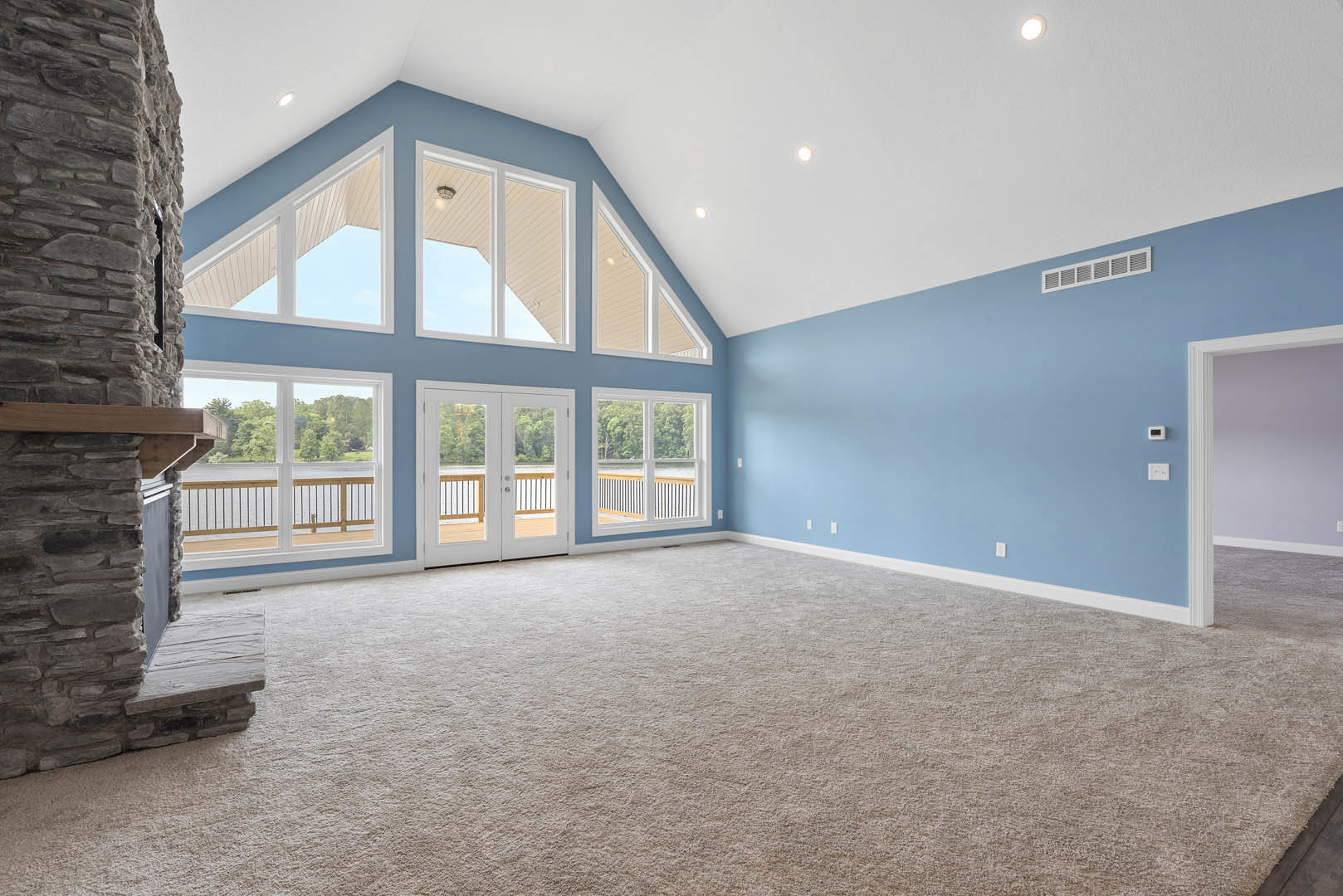 Carpeted living space featuring blue accent wall, multiple windows, stone fireplace with wooden mantel, white ceiling, and white door.