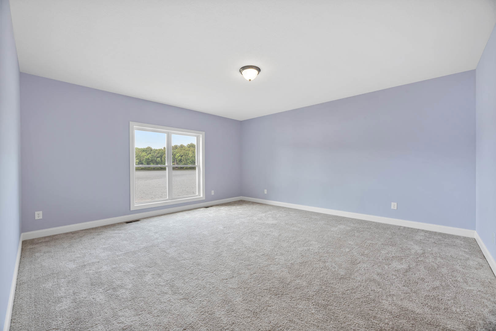 Carpeted room with white walls, ceiling light fixture, large window overlooking lake and trees