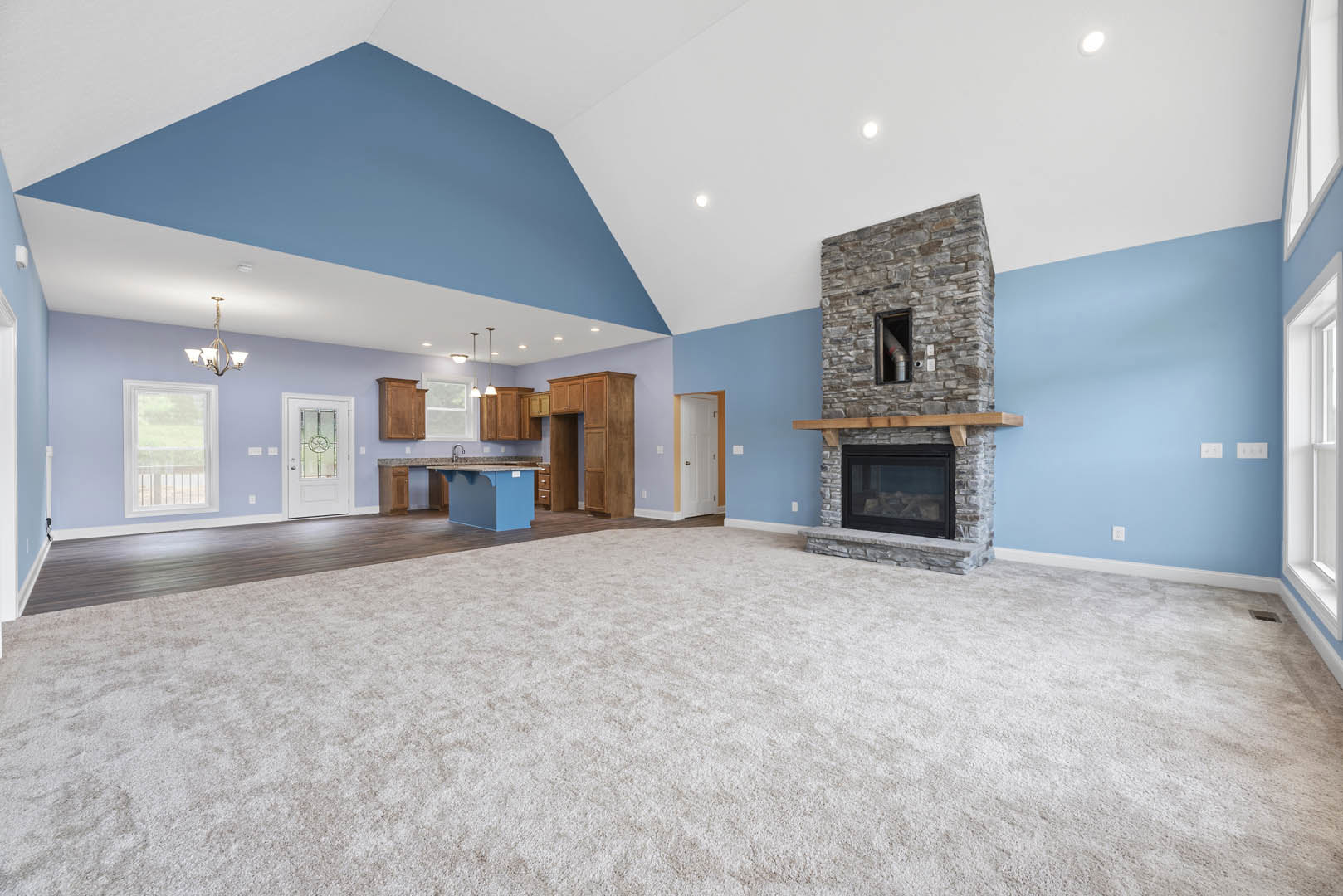 Spacious living room with beige carpet, central fireplace featuring a glass door and vent, open kitchen area, white door with glass panel, and window with metal railing
