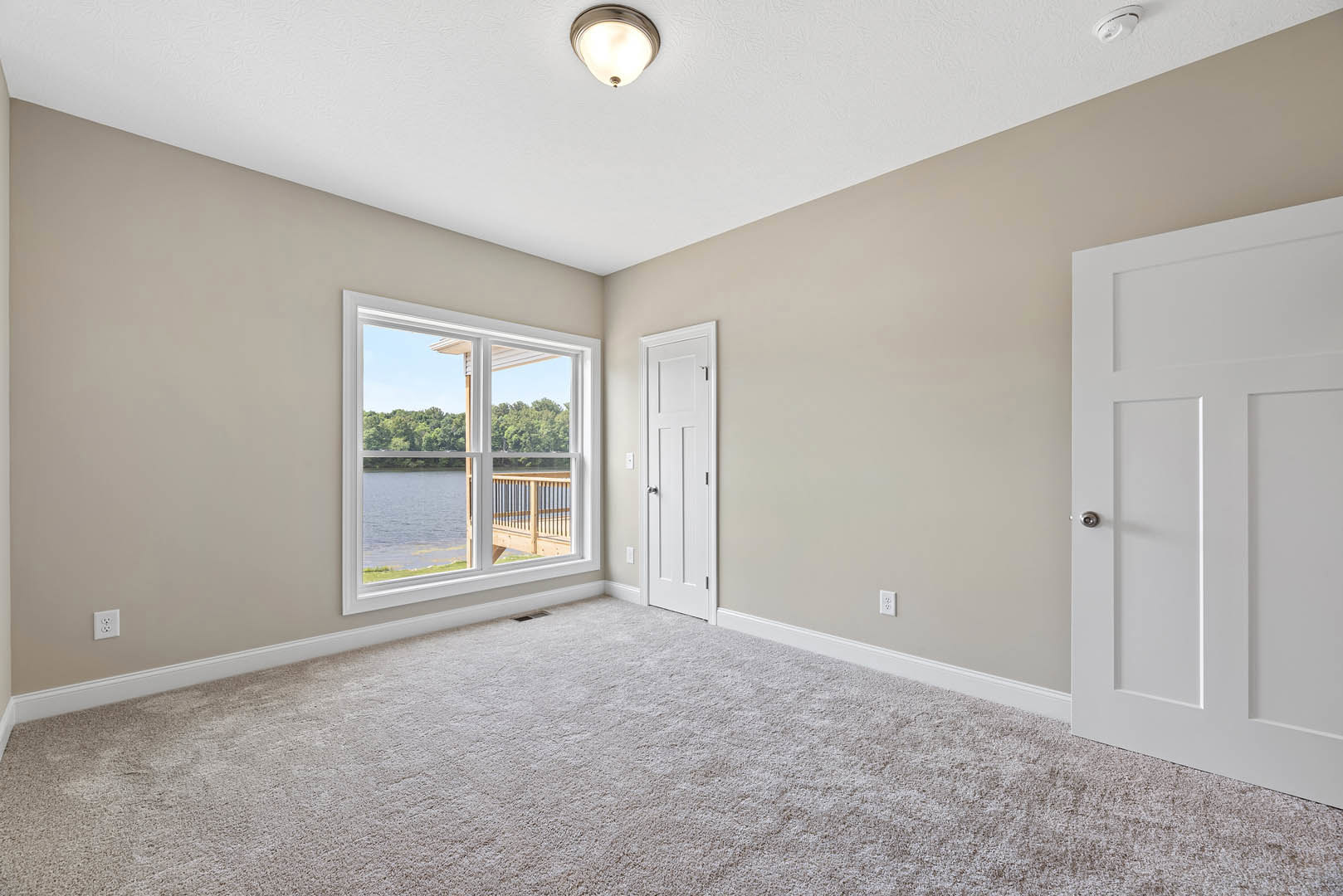 Carpeted room with white walls, white door featuring a silver knob, ceiling light fixture, and window overlooking a lake