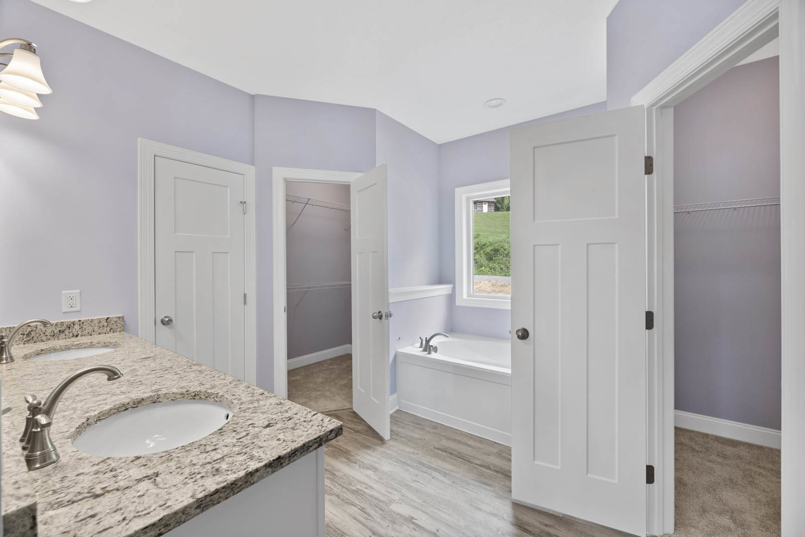 White paneled doors with black handles, freestanding bathtub, tiled walls, modern sink and faucet, wall-mounted lamp, large mirror, and built-in cabinetry