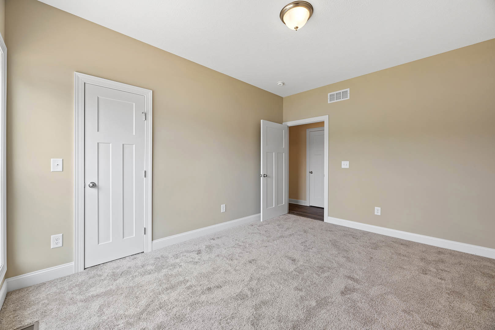Beige carpeted floor, white paneled doors with silver handles, white walls, ceiling-mounted light fixture, white electrical outlet with black button