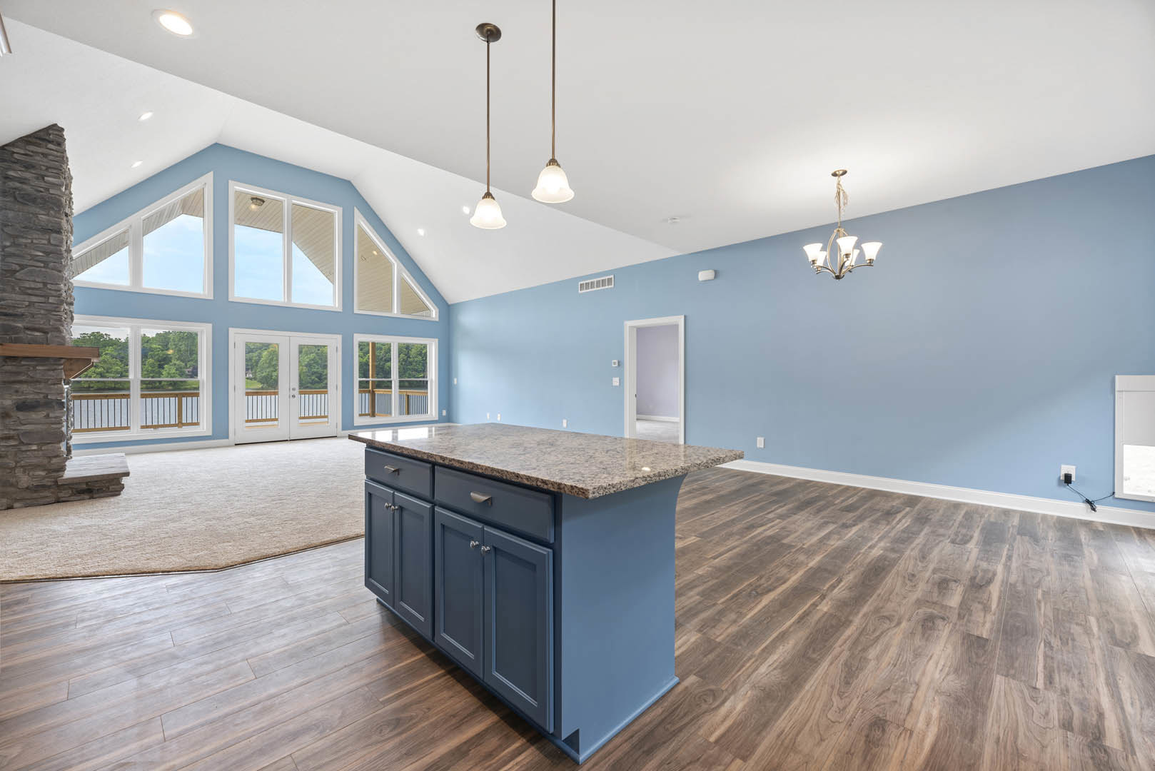 Open-concept kitchen with granite island, wood flooring, blue accent wall, white door, modern chandelier, and white cabinetry