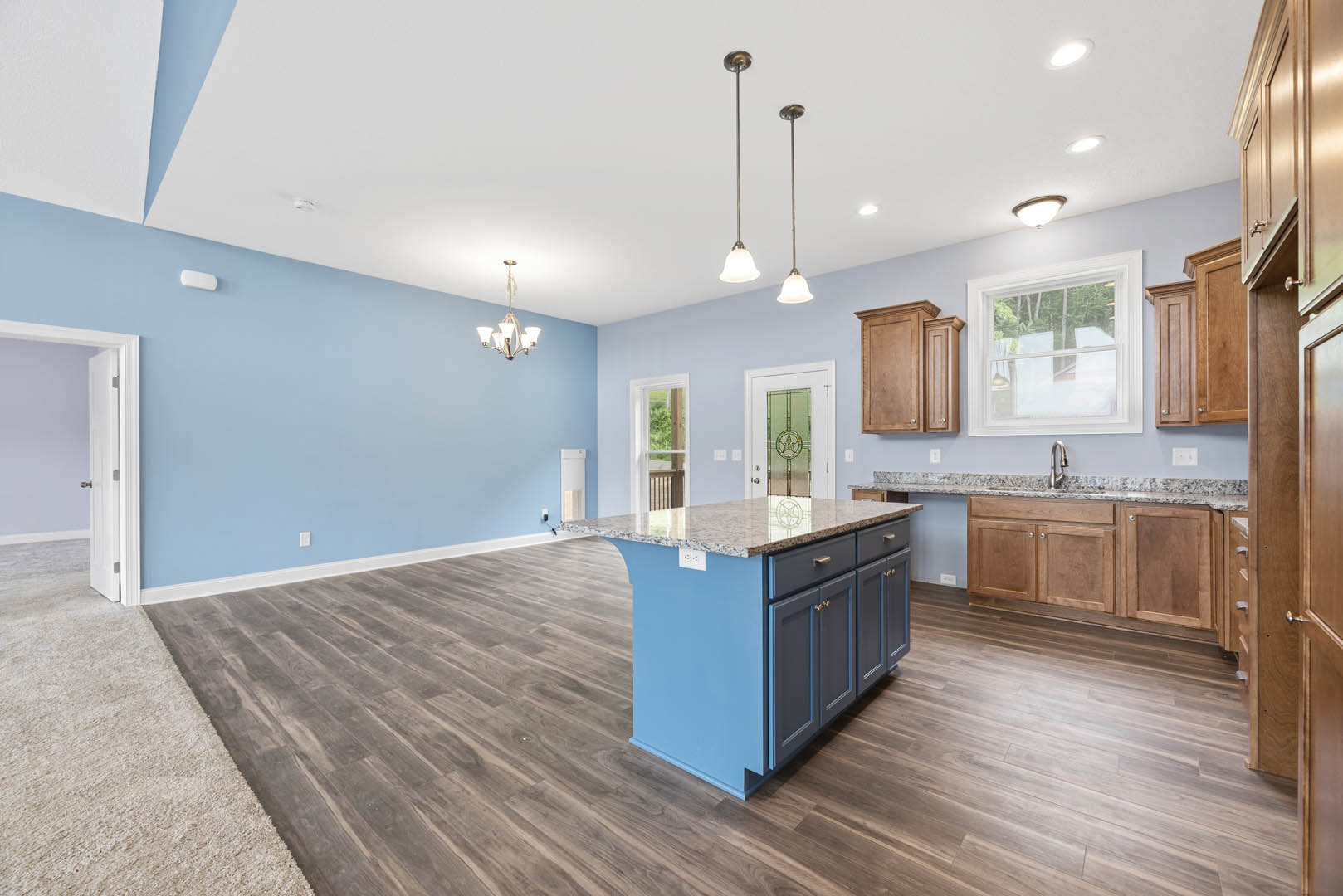 Marble kitchen island with waterfall edge, wood plank flooring, white cabinetry, stainless steel sink, pendant light fixtures, large window with white trim