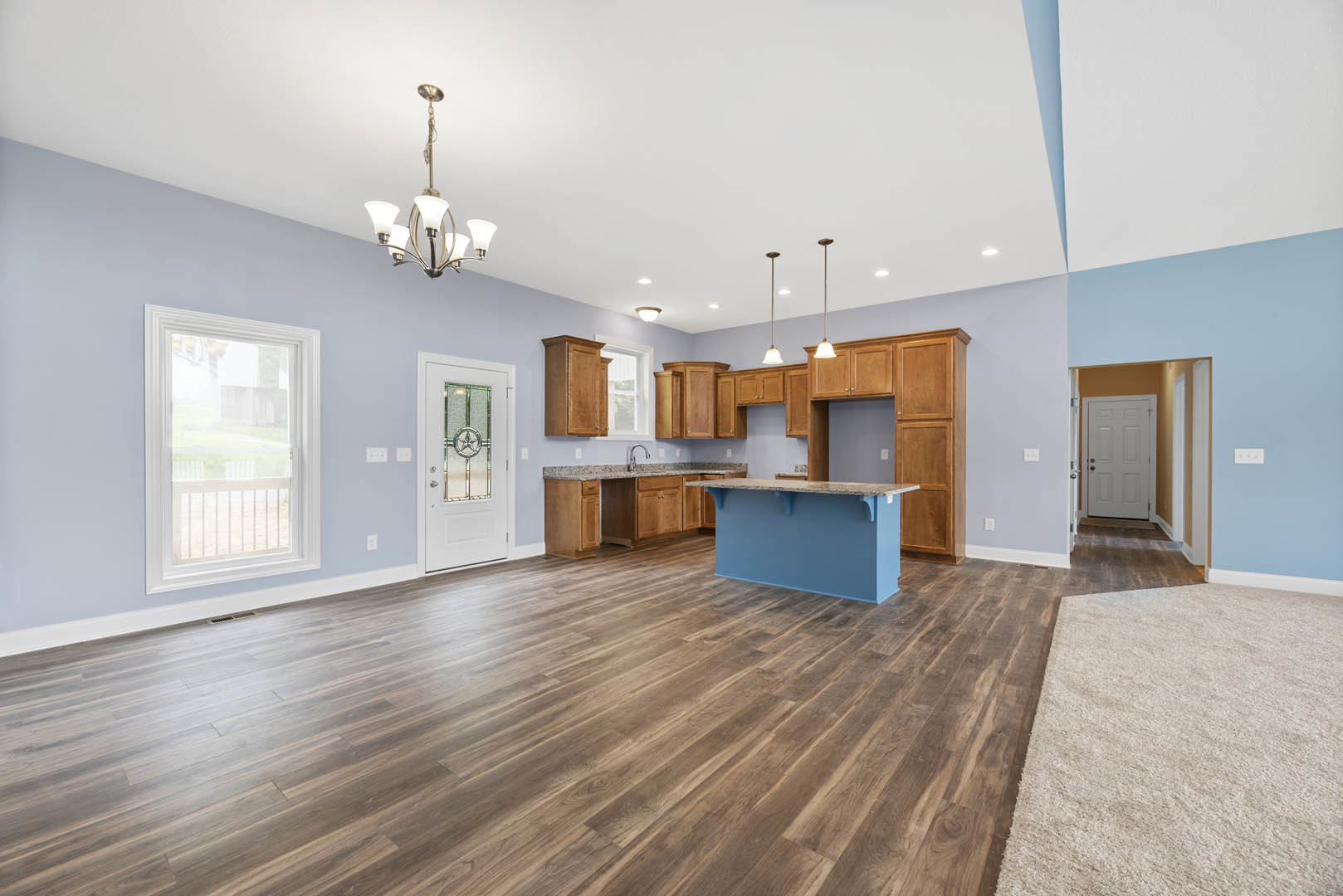 Spacious open floor plan featuring a central kitchen island with marble countertop, hardwood flooring throughout, blue accent wall, white framed window with railing, and white