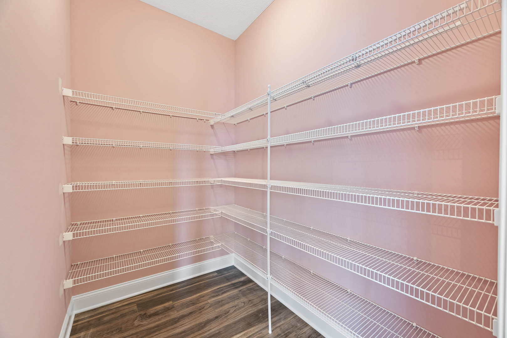 Empty closet with white built-in shelves, pink walls, and wood flooring with white baseboard
